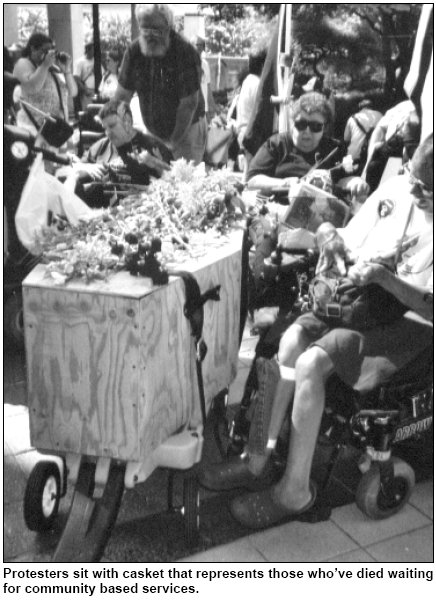Protesters sit with casket that represents those whove died waiting for community based services.